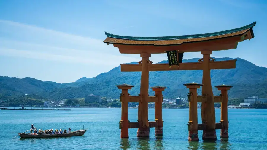 The floating torii gate of Miyajima Island near Hiroshima, with a traditional boat passing beneath a blue sky