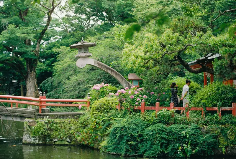 Couple walking through a traditional Japanese garden with a red bridge and stone lantern