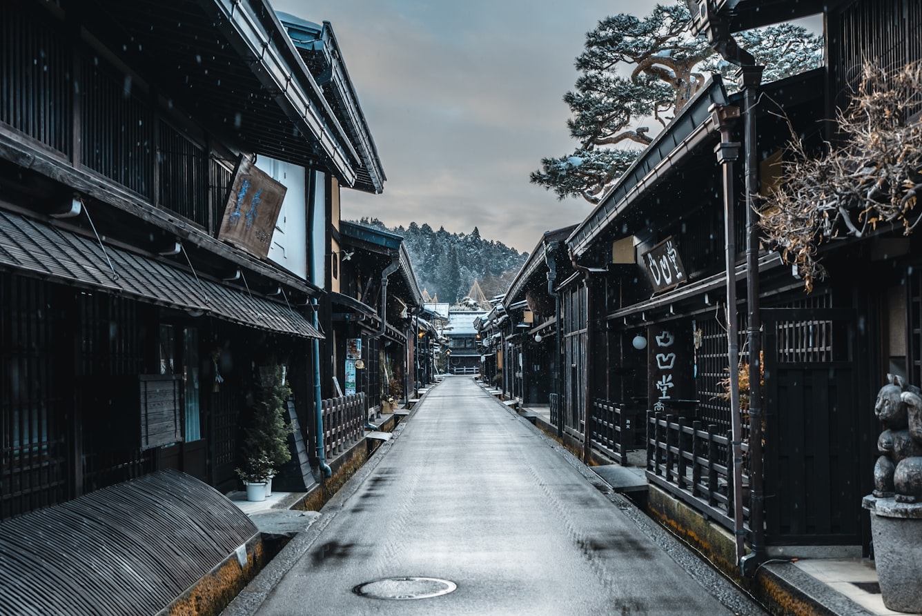 The dark-timbered merchant houses of Takayama's old town under falling snow