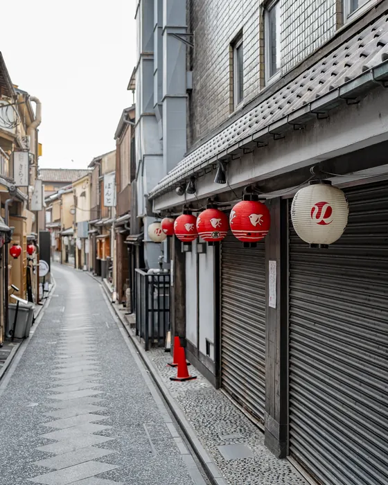 A quiet lane in Gion, Kyoto, at dawn, red lanterns hanging from the wooden houses